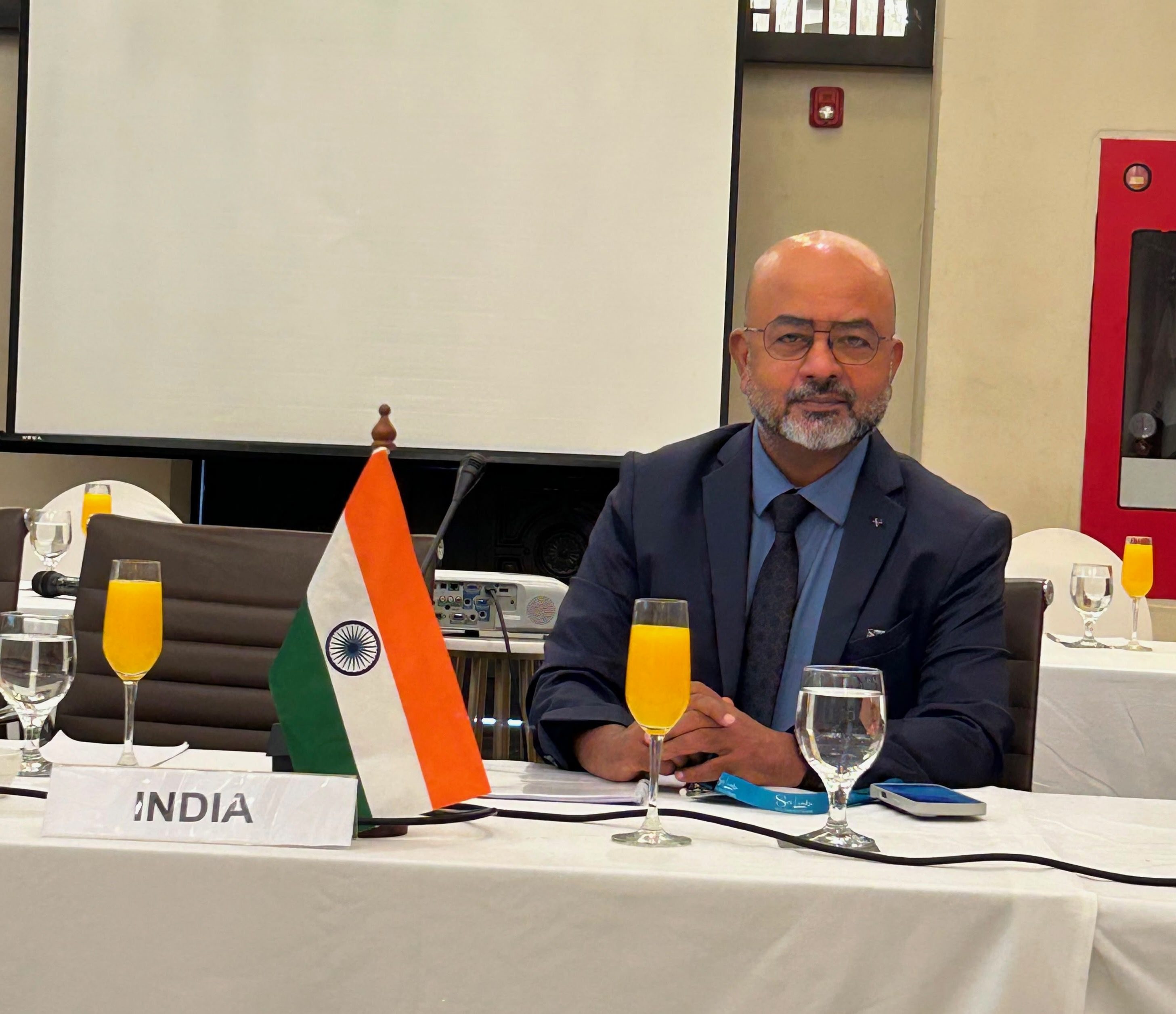 Sunil Mishra seated at a meeting table beside an India flag